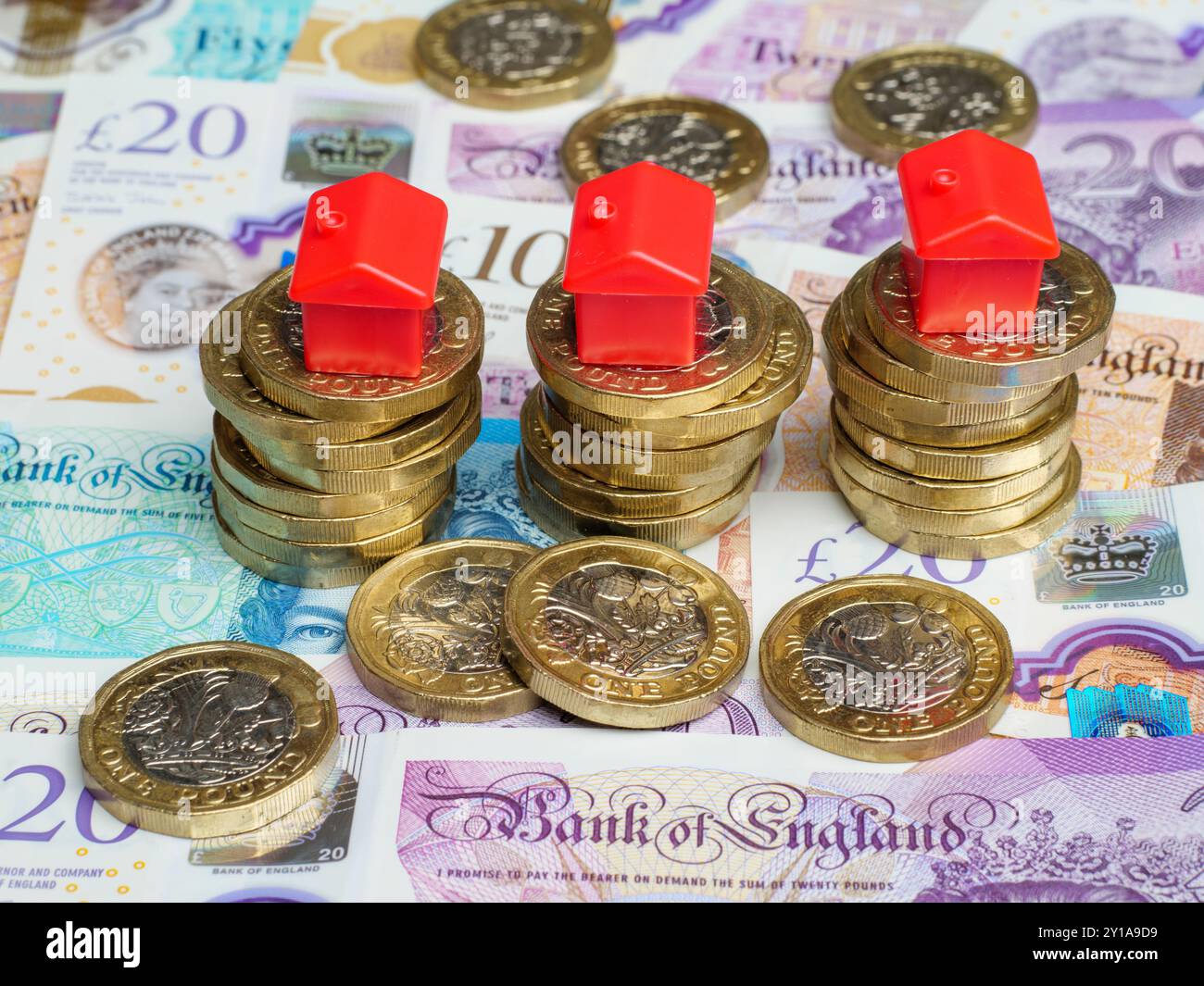 Nahaufnahme von Häusern aus Kunststoff, die auf Stapeln von britischen Pfund-Münzen und Pfund-Banknoten platziert wurden, Geld Bargeld, Großbritannien Stockfoto
