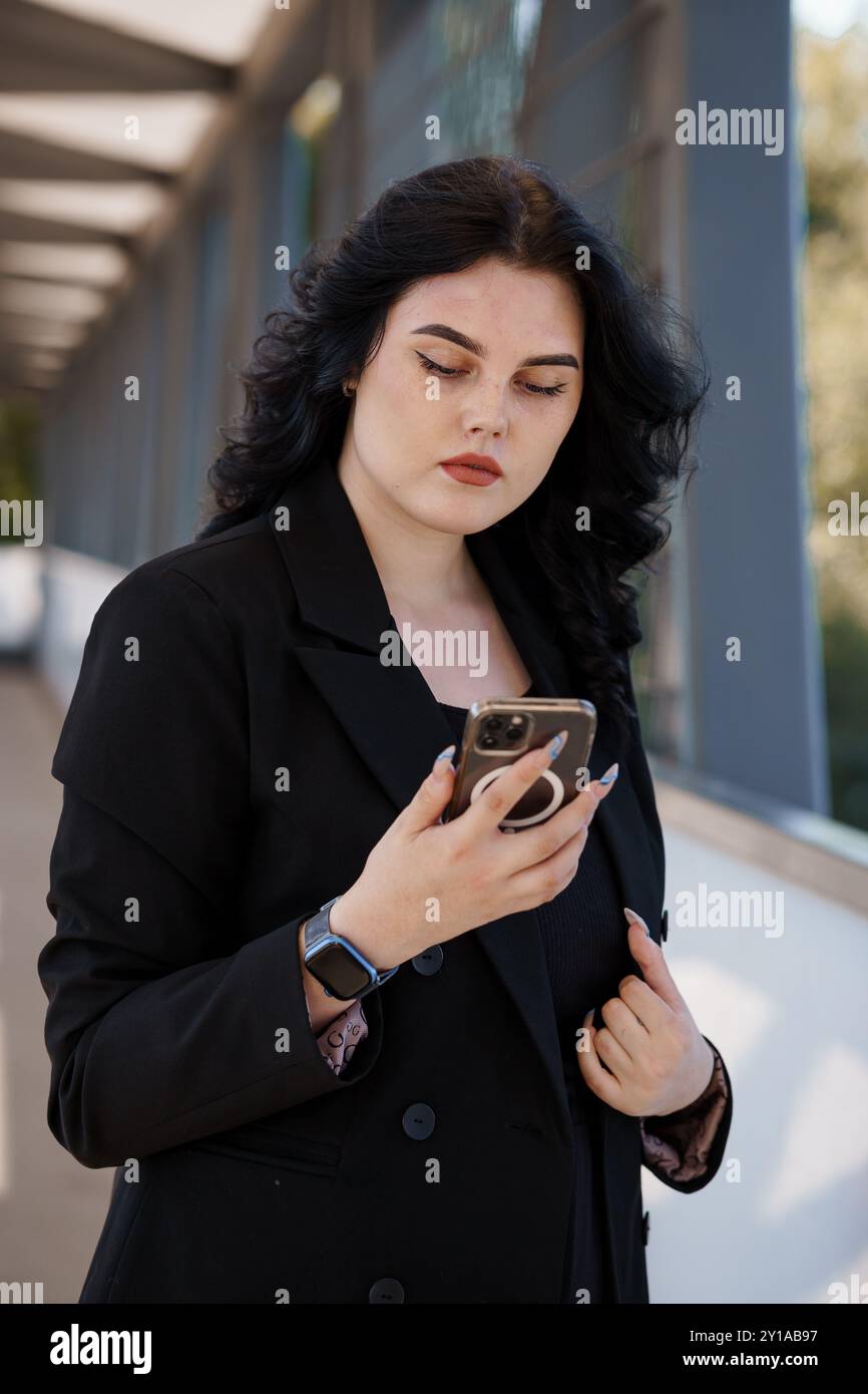 Selbstbewusste junge Profi-Frau, die draußen auf dem Smartphone SMS schreibt. Stockfoto