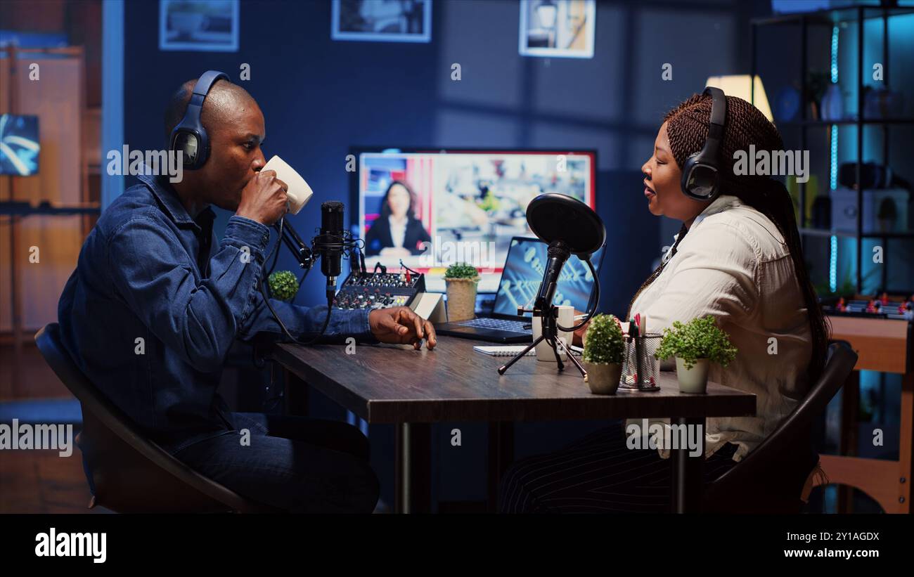 Zeigen Sie den Host, der Podcast aufnimmt, genießen Sie eine Tasse Kaffee und nette Gespräche mit den Gästen. afroamerikanischer Mann, der professionelle Audiogeräte für eine einwandfreie Klangqualität verwendet, während er mit einer Frau im Live-Chat spricht Stockfoto