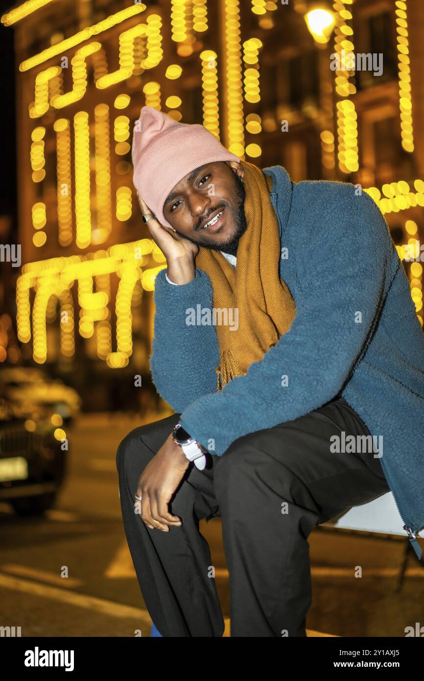 Vertikales Porträt eines coolen afrikaners, der in einer Weihnachtsnacht in der Stadt sitzt Stockfoto