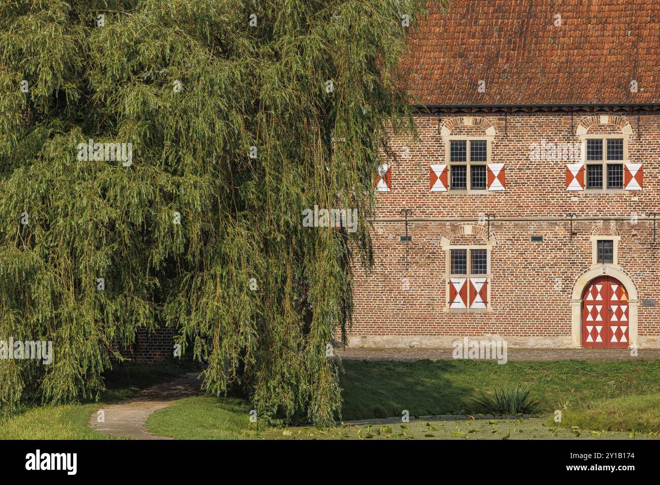 Backsteingebäude mit Rollläden und rotem Dach, neben einer großen Weide und einem Weg, Raesfeld, Münsterland, Deutschland, Europa Stockfoto