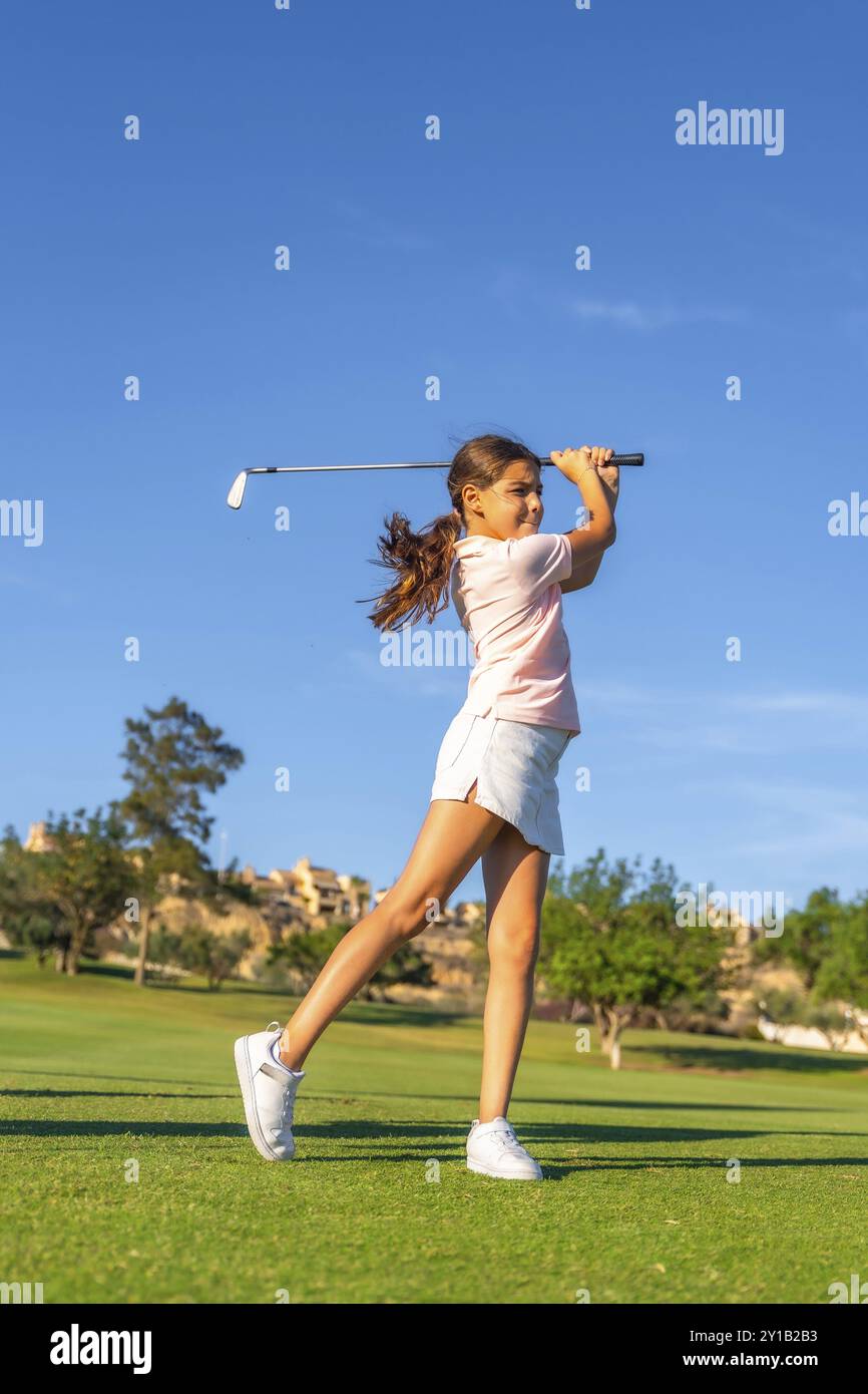 Vertikales Foto in voller Länge von einem blonden Mädchen, das im Sommer auf einem Golfplatz im Freien Golf schwingt Stockfoto