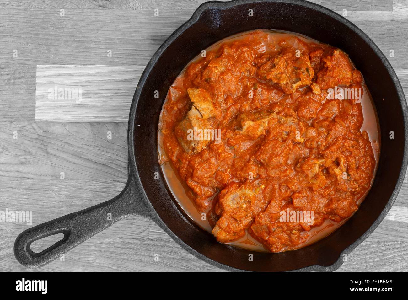 Rogan josh Lammcurry in einer gusseisernen Pfanne gekocht. Auf hölzernem Hintergrund Stockfoto