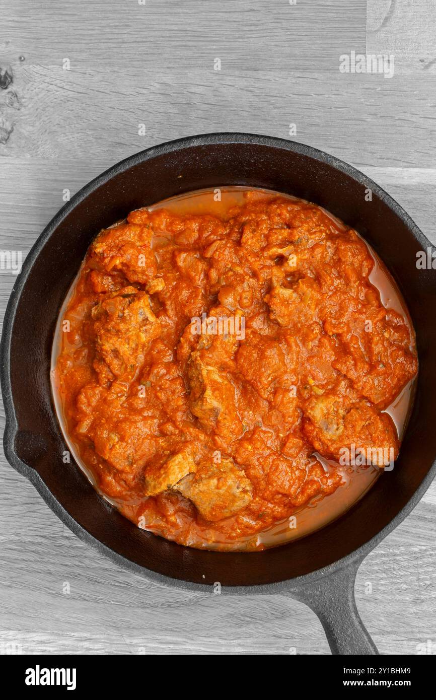 Rogan josh Lammcurry in einer gusseisernen Pfanne gekocht. Auf hölzernem Hintergrund Stockfoto