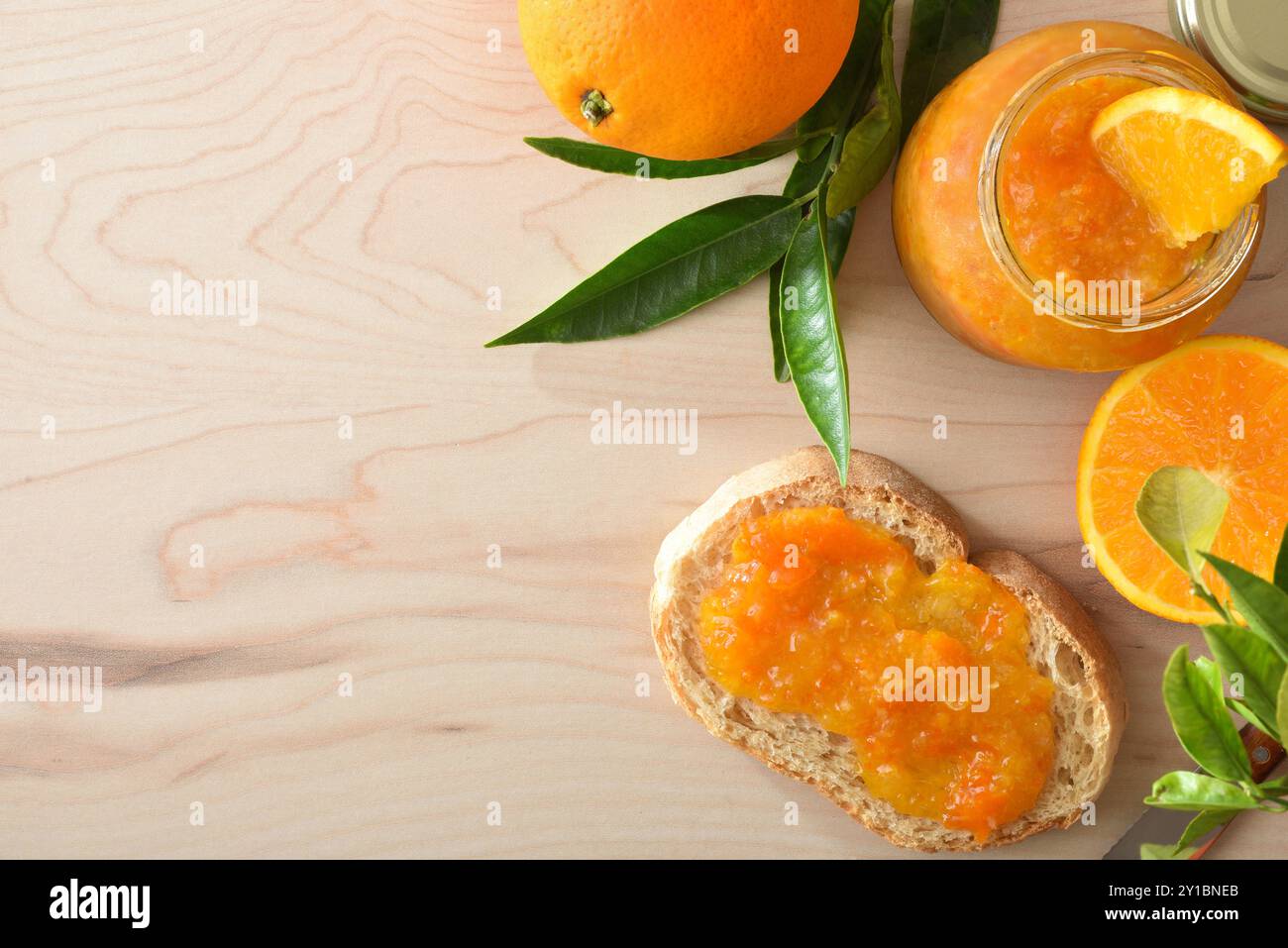 Hausgemachte Orangenmarmelade im Glasgefäß und Toast auf Holztisch mit Obststücken herum. Draufsicht. Stockfoto