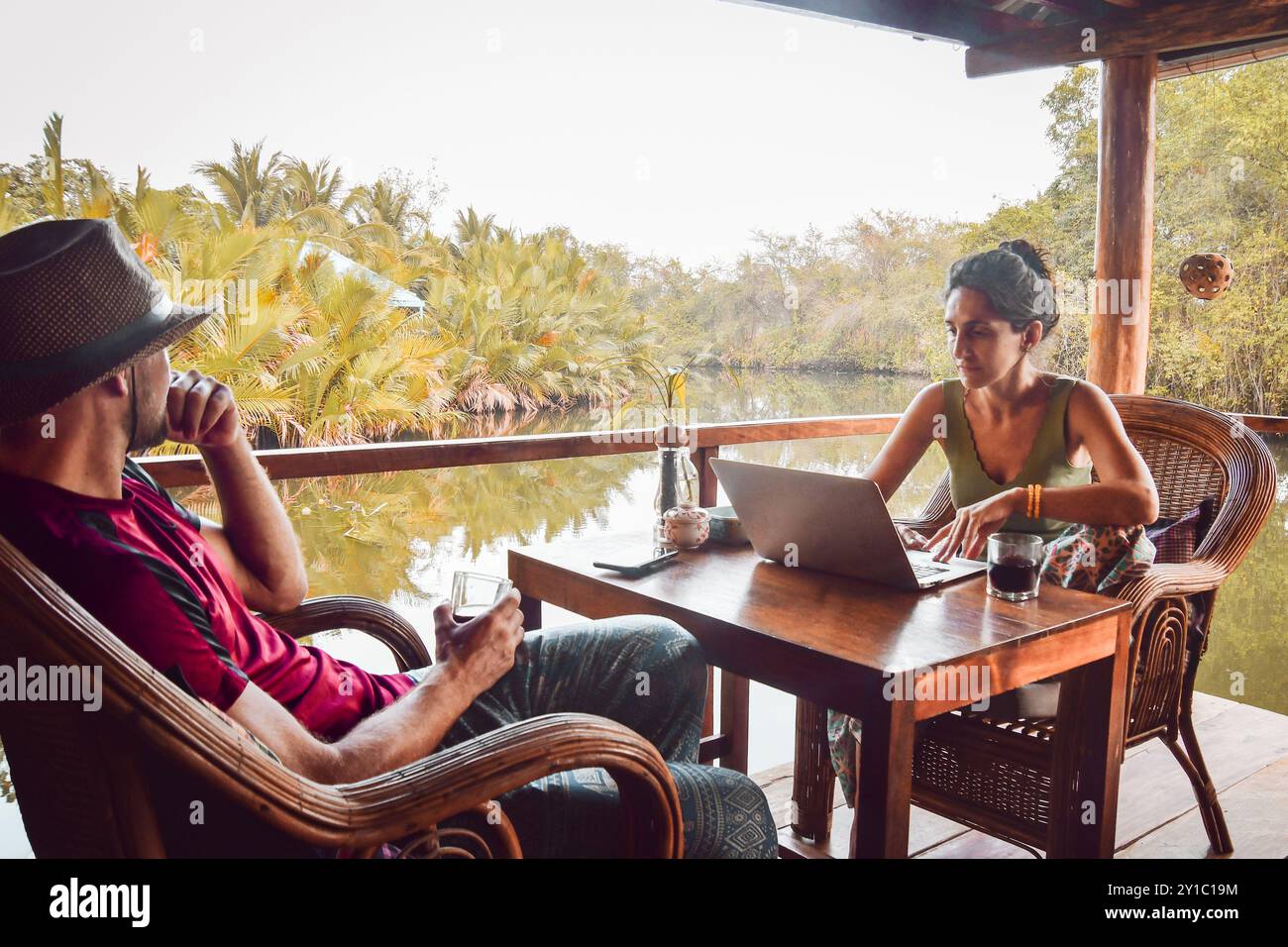Nahaufnahme Hipster Digital Nomaden Paar sitzen im Café mit Laptop-Arbeit online am malerischen Fluss und Palmen in südostasien Stockfoto