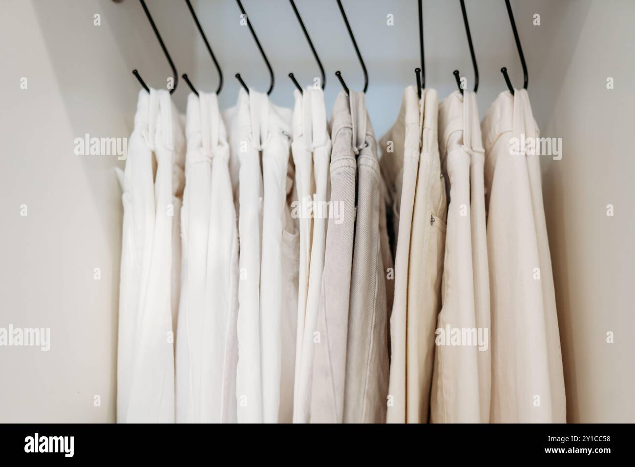 Weiße und cremefarbene Jeans hängen an Haken im Schrank Stockfoto