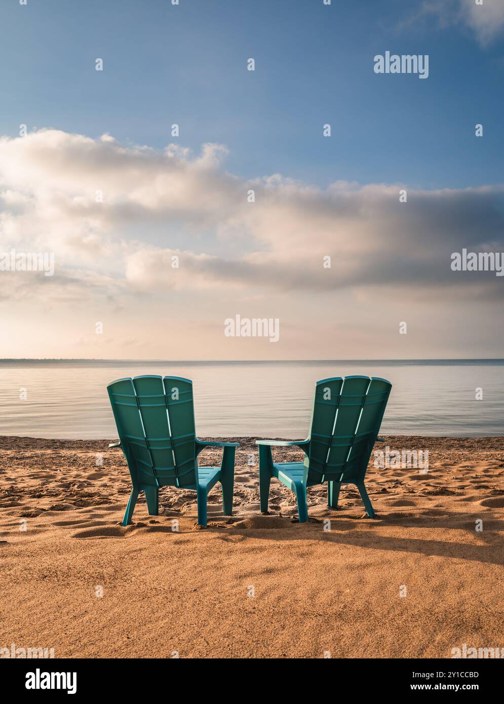 Zwei blaue adirondack-Stühle am Sandstrand mit Blick auf den See im Sommer. Stockfoto