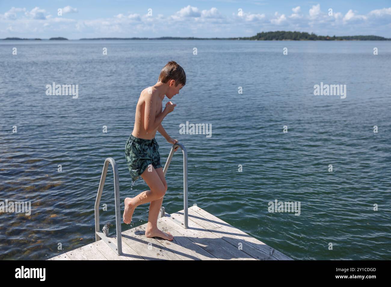 Junge klettert aus dem See auf einem Metallleiterdock Stockfoto