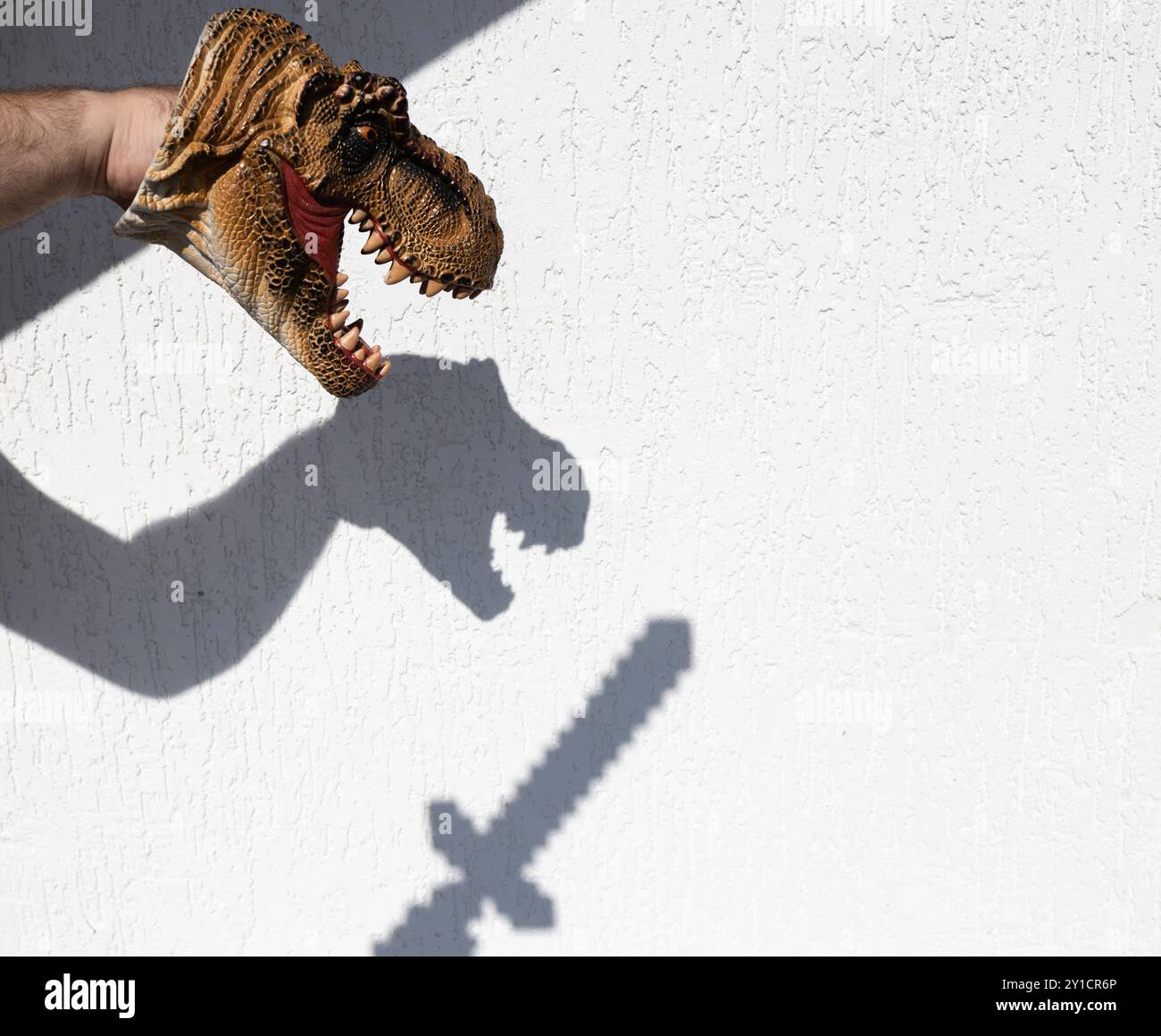 Schattentheater. Silhouette eines Dinosaurierkopfes und eines Schwertes gegen eine weiße Wand. Interessante kontrastierende Schatten an der Wand. Ideen für Schattenspiele, d Stockfoto