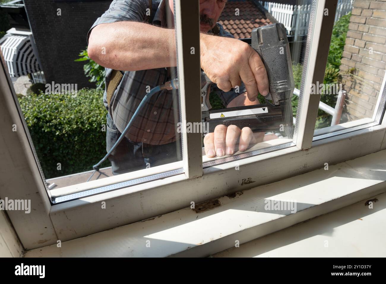 Zimmermann mit Nagelpistole befestigt Glasperlen an einem neuen doppelt verglasten Fenster mit Stangenteilung. Renovierung eines älteren Hauses Stockfoto