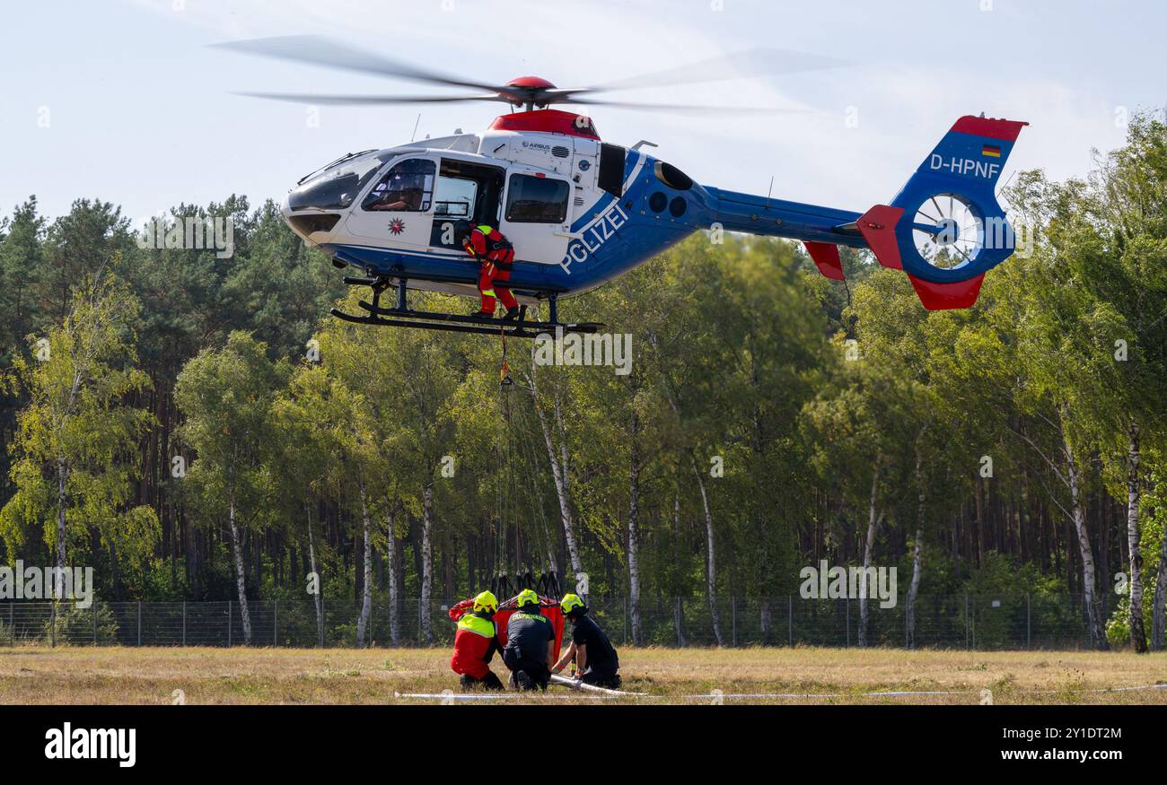 Bleckede, Deutschland. September 2024. Während einer Waldfeuerbekämpfung erhalten freiwillige Feuerwehrleute Anweisungen, wie sie einen Löschwassertank, den sogenannten Bambi-Eimer, in einem Polizeihubschrauber füllen. Freiwillige Feuerwehrleute der Niedersächsischen Feuerwehr übten den Einsatz von zwei Hubschraubern zur Bekämpfung von Vegetationsbränden. Quelle: Philipp Schulze/dpa/Alamy Live News Stockfoto