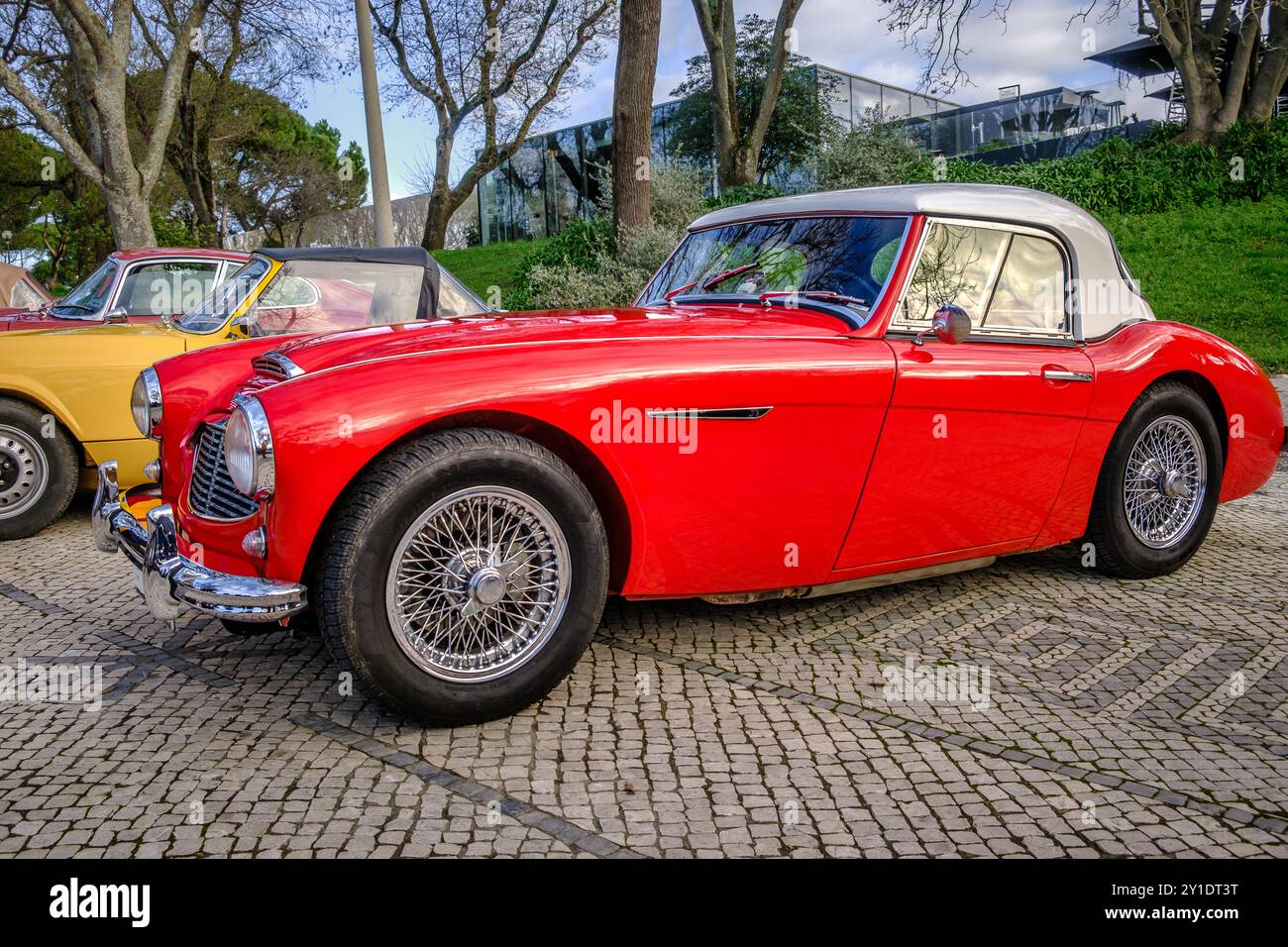 Lissabon, Portugal - 20. Januar 2024: Roter Austin Healey 100-6 Roadster auf Kopfsteinpflaster in der Nähe des grünen Parks Stockfoto