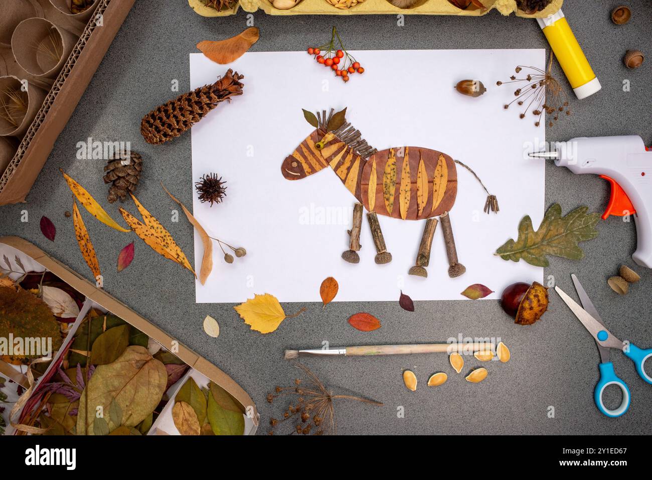 Bastelprojekt zum Thema „DIY Animal Herbstmotiv“ mit Zebras, die mit Blättern und Zweigen ausgeschnitten wurden, umgeben von Bastelmaterialien wie Herbstlaub, Beeren und Pin Stockfoto