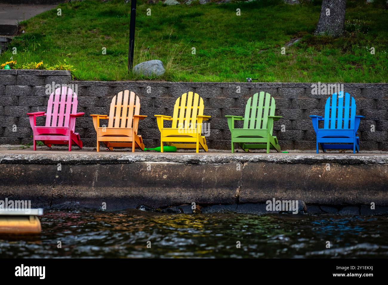 Bunte Adirondack-Stühle auf einem Concreate-Dock im Sommer, horizontal Stockfoto