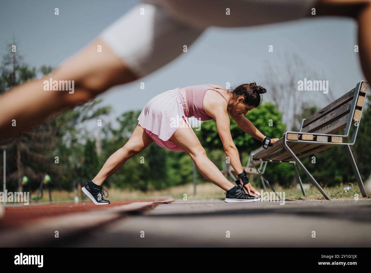 Frau, die sich im Park ausdehnt, während sie sich während des Aufwärmens auf eine Bank lehnt Stockfoto