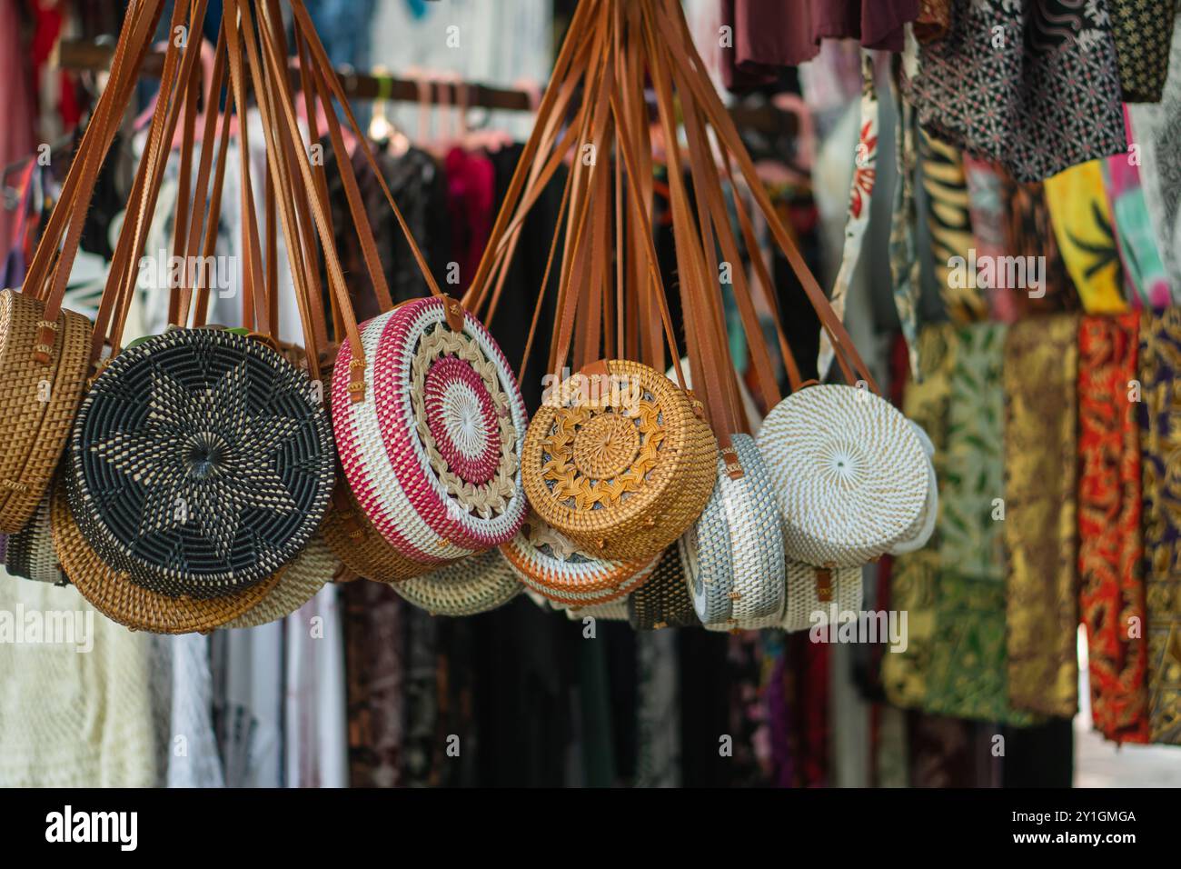 Eine lebendige Ausstellung handgemachter runder gewebter Taschen, die auf einem Markt hängen. Die Taschen haben komplizierte Designs und farbenfrohe Muster, umgeben von verschiedenen Tischen Stockfoto