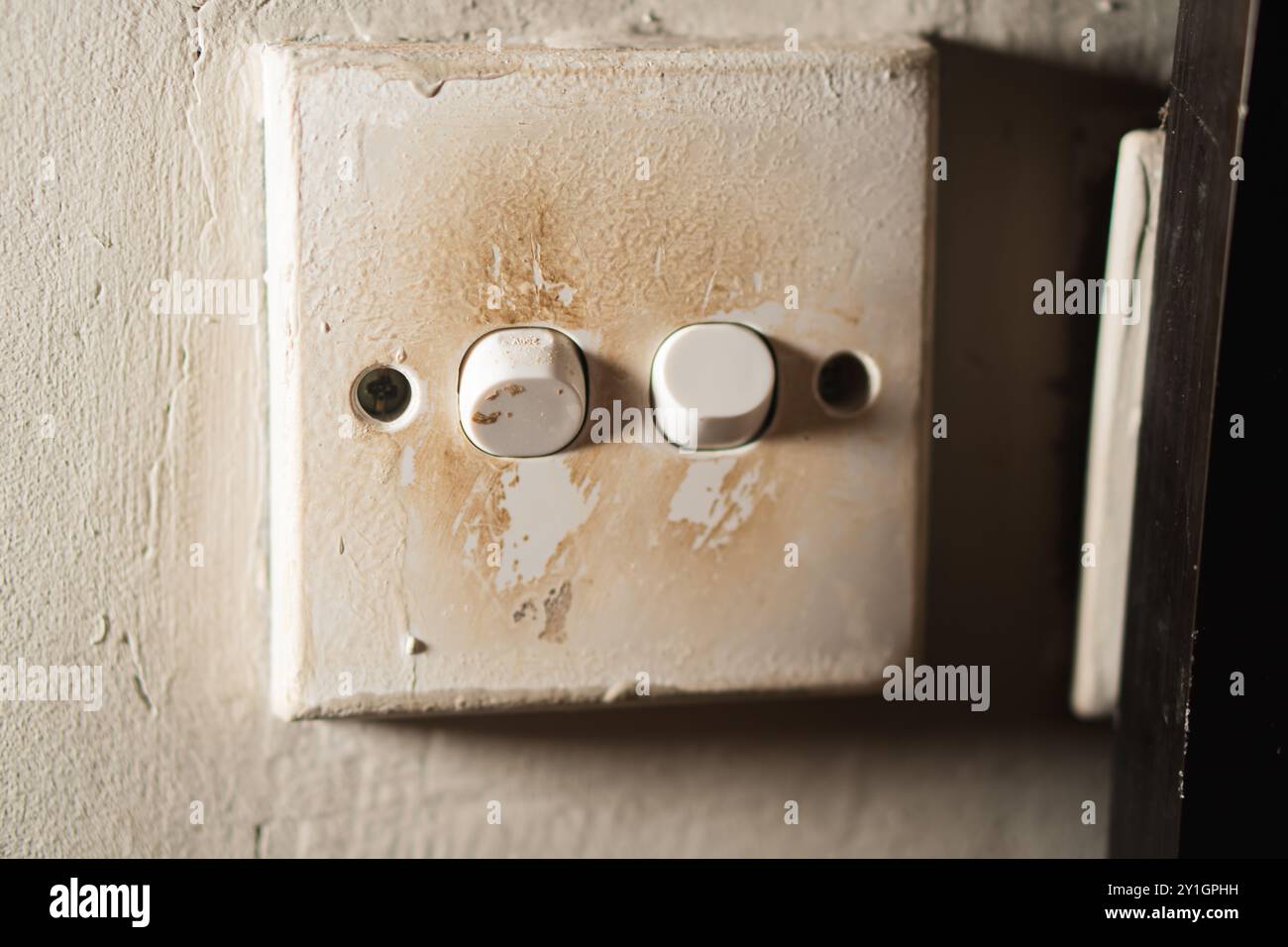 Eine Nahaufnahme eines schmutzigen, abgenutzten Lichtschalters an einer Wand. Die Schalterplatte ist mit Flecken verfärbt, und die Schalter sind leicht verblasst. Der Text an der Wand Stockfoto