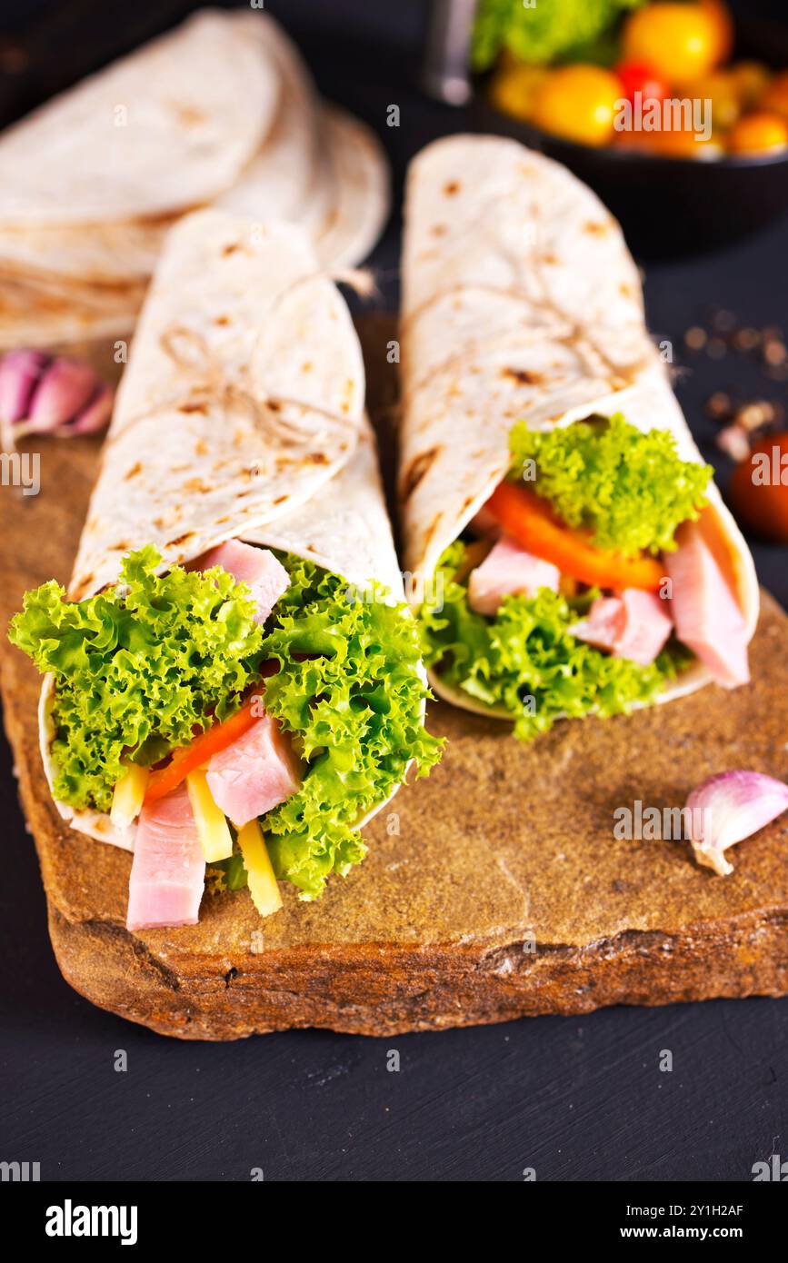 Frische Tortilla Wraps mit Schinken, Käse und Gemüse auf Steinbrett Stockfoto