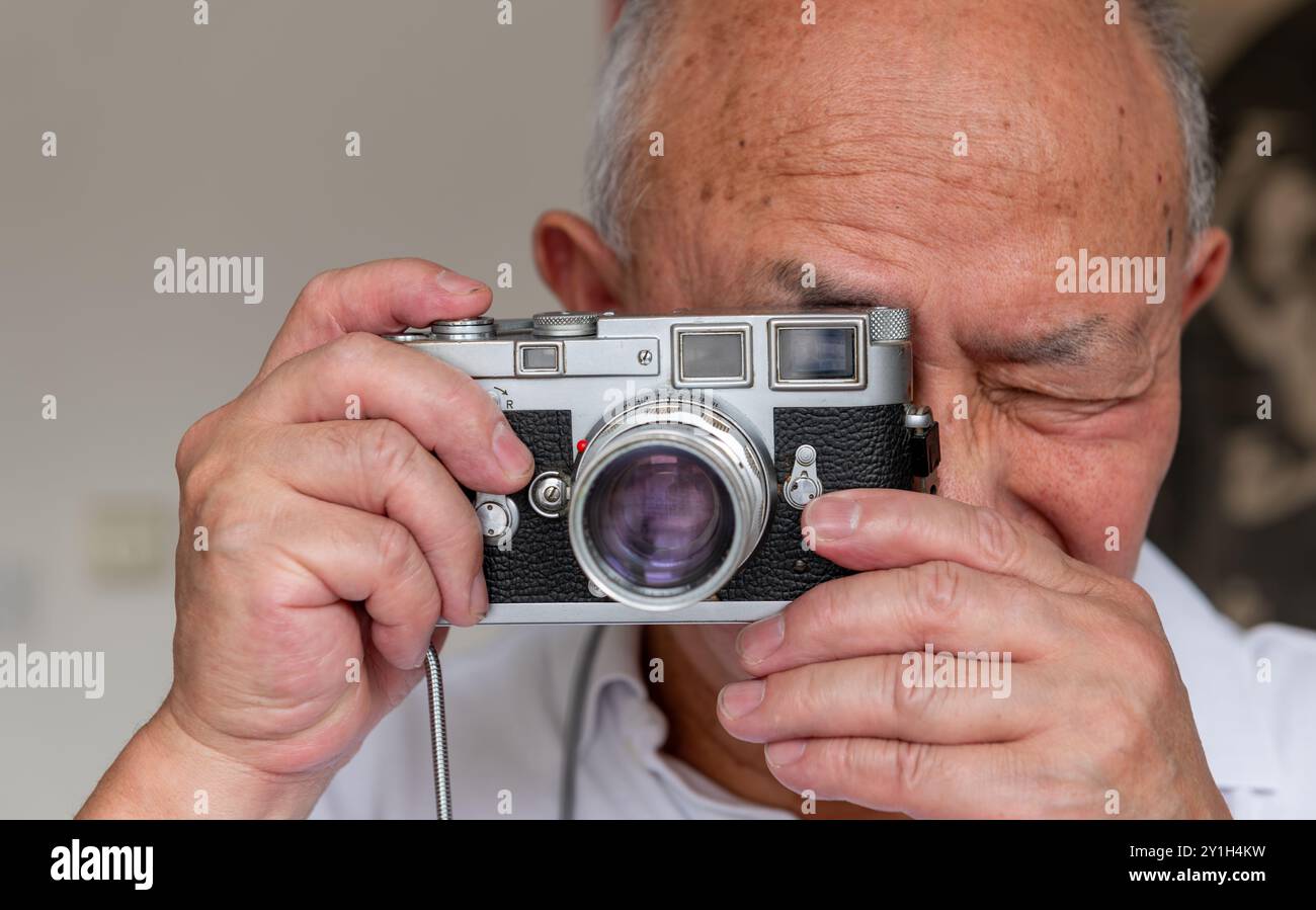 Ein älterer Mann, der eine klassische Vintage-Kamera benutzt, um Fotos zu machen. Stockfoto