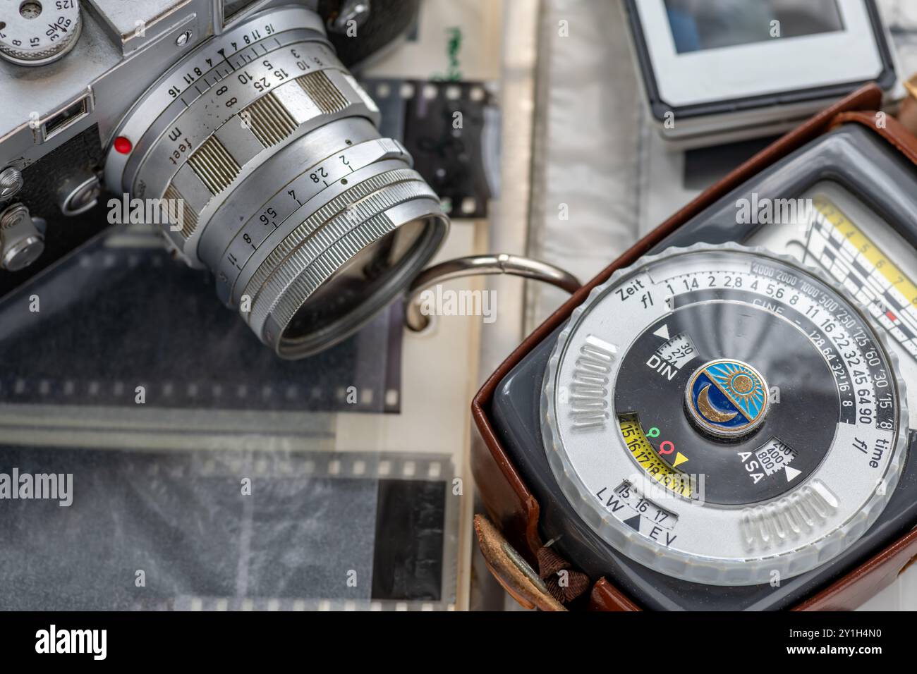 Nahaufnahme eines Lichtmessers für die Vintage-Fotografie und einer Vintage-Kamera auf einem Ordner mit Filmnegativen und Dias. Stockfoto