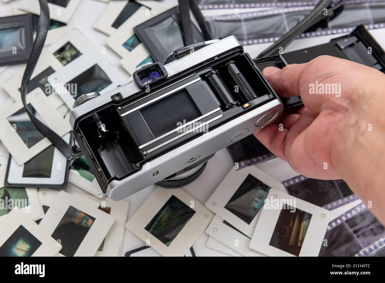 Eine Person, die die geöffnete Rückseite einer alten Spiegelreflexkamera auf einem Stapel Dias und Filmnegative hält. Stockfoto