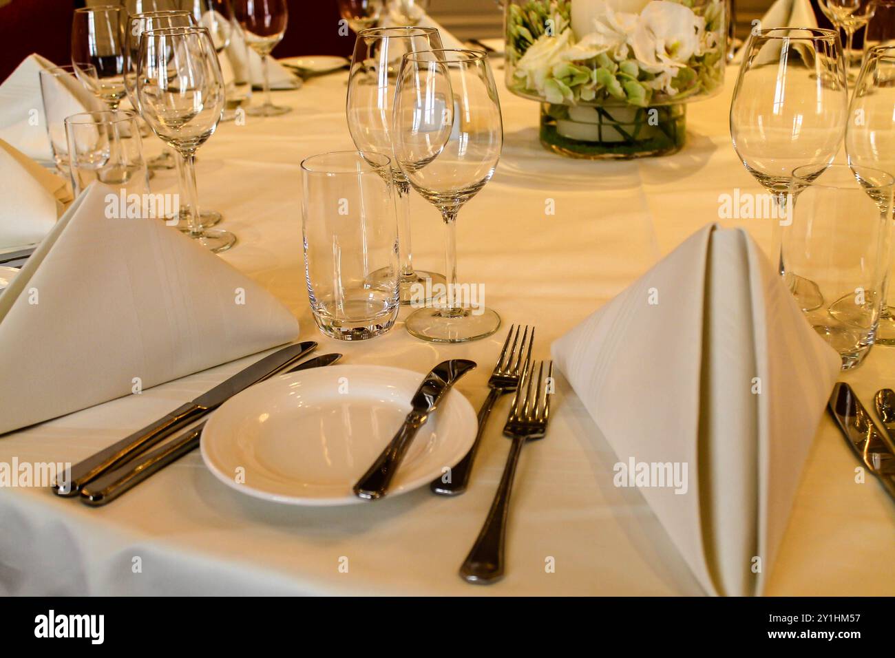 Ein wunderschön gedeckter Esstisch mit eleganten weißen Servietten, Gläsern und Besteck, ordentlich angeordnet. Das Herzstück ist mit frischen Blumen versehen, die einen Stockfoto