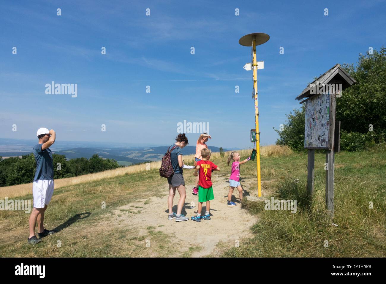 Familie von Wanderern, die an einem sonnigen Tag an einem Wegkreuz mit Wegweisern und Karten stehen und einen malerischen Blick auf die Landschaft bieten Stockfoto