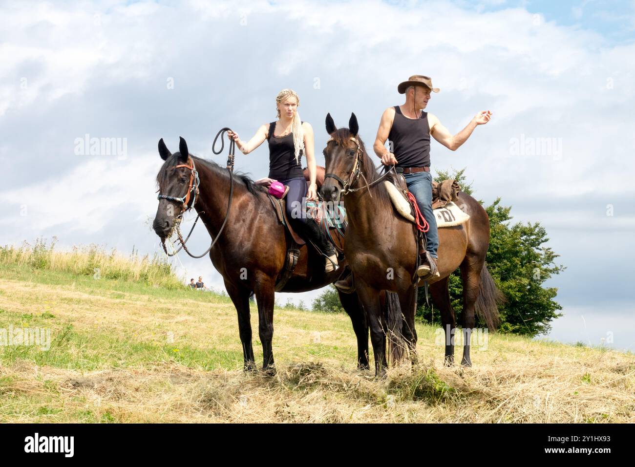 Ein Mann und eine Frau reiten Pferde auf einem grasbewachsenen Feld unter bewölktem Himmel an einem sonnigen Tag Stockfoto