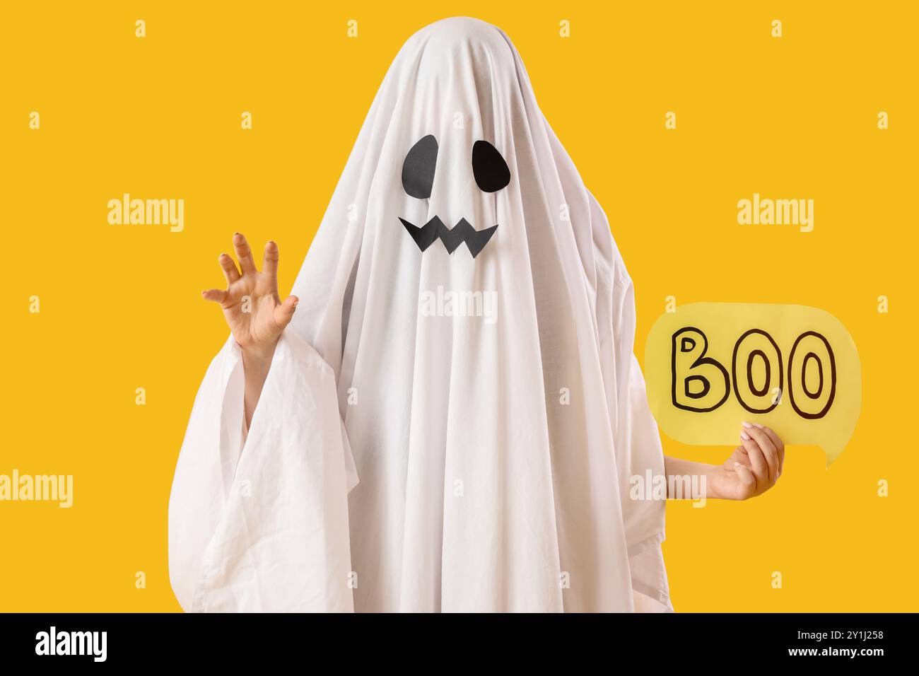 Person im Halloween-Kostüm eines Geisters, der Sprechblase mit Wort BUH auf gelbem Hintergrund hält Stockfoto