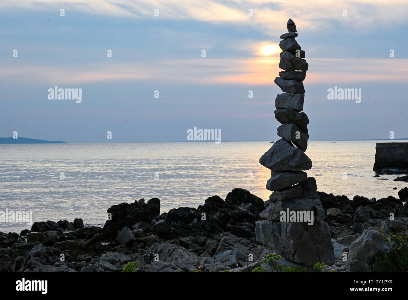 Ein hoher Steinhaufen ist am felsigen Strand eines Ozeans ausgeglichen, während die Sonne in der Ferne untergeht. Stockfoto