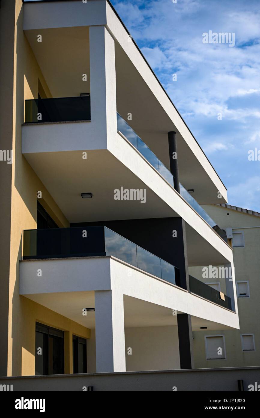 Geometrische Formen eines weißen modernen Gebäudes mit Balkonen mit Glasgeländern unter blauem Himmel. Stockfoto