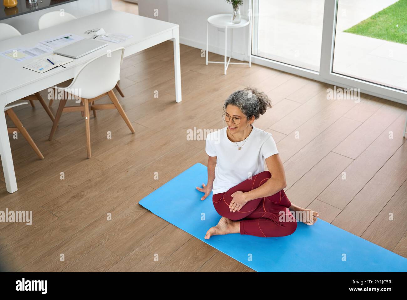Glückliche, gesunde Frau mittleren Alters, die Yoga-Übungen macht, zu Hause sitzend. Stockfoto