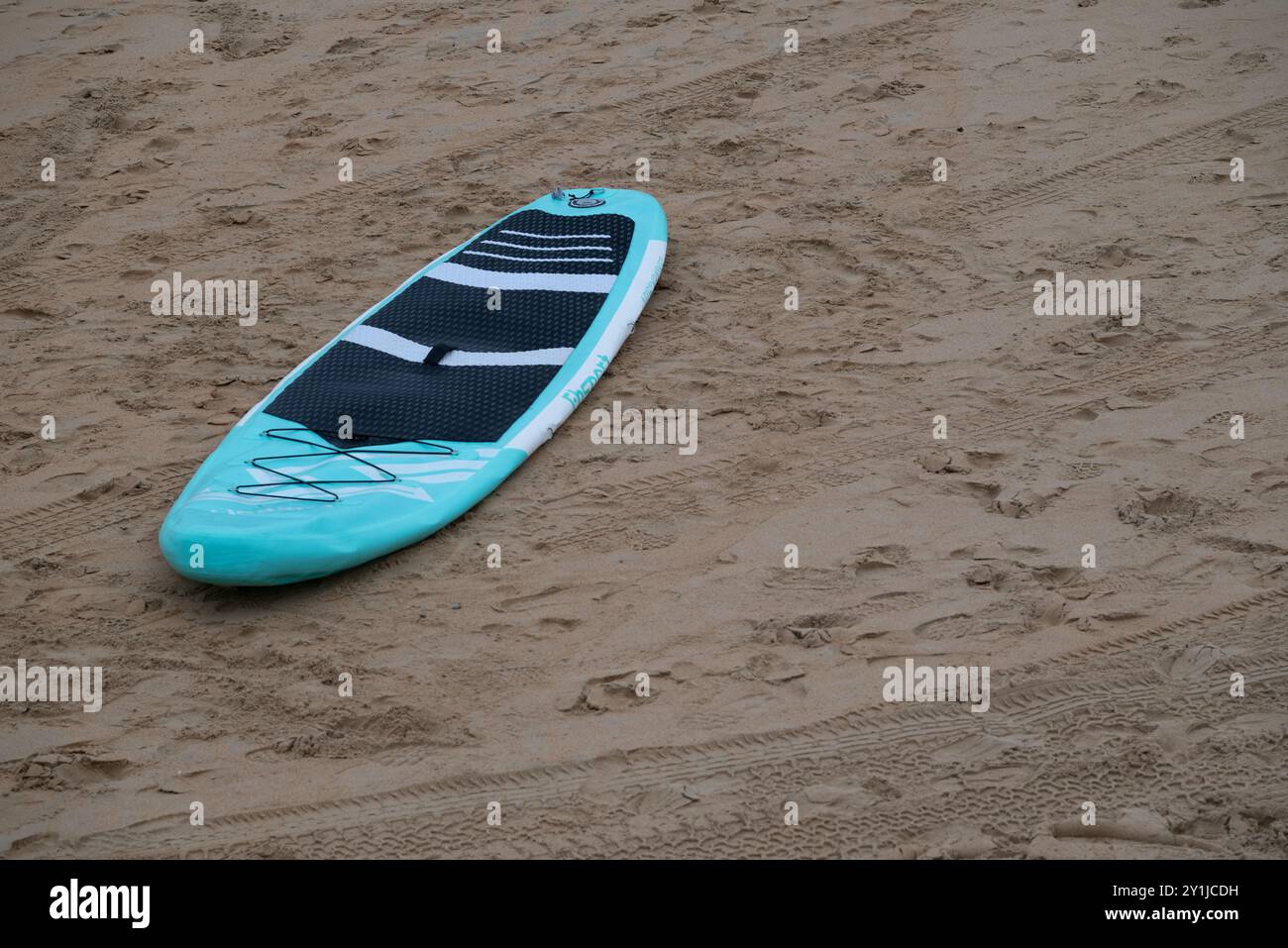 Hellblaues Paddelbrett am Strand von La Concha in San Sebastian im baskenland, Spanien. Mit sichtbaren Fahrzeugspuren und Fußmarkierungen Stockfoto