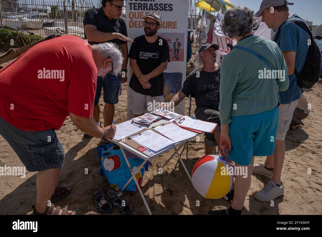 Demonstranten, die am Tisch unterschrieben werden, sammeln Petitionen gegen das große Sportereignis des America's Cup Segelsports. Hundert Aktivisten und Einwohner Barcelonetas haben am Strand von Somorrostro in Barceloneta eine Menschenkette gebildet, um gegen die Segelveranstaltung des America's Cup zu protestieren. Nach Aussagen der Demonstranten untergräbt die Veranstaltung dieses großen Sportereignisses die Integrität der Arbeiterviertel, ignoriert Forderungen nach sofortigen Maßnahmen zur Verringerung der Tourismuswirtschaft und enteignet den Bürgern massiv den öffentlichen Raum. All das ohne wirtschaftliche zu bringen Stockfoto