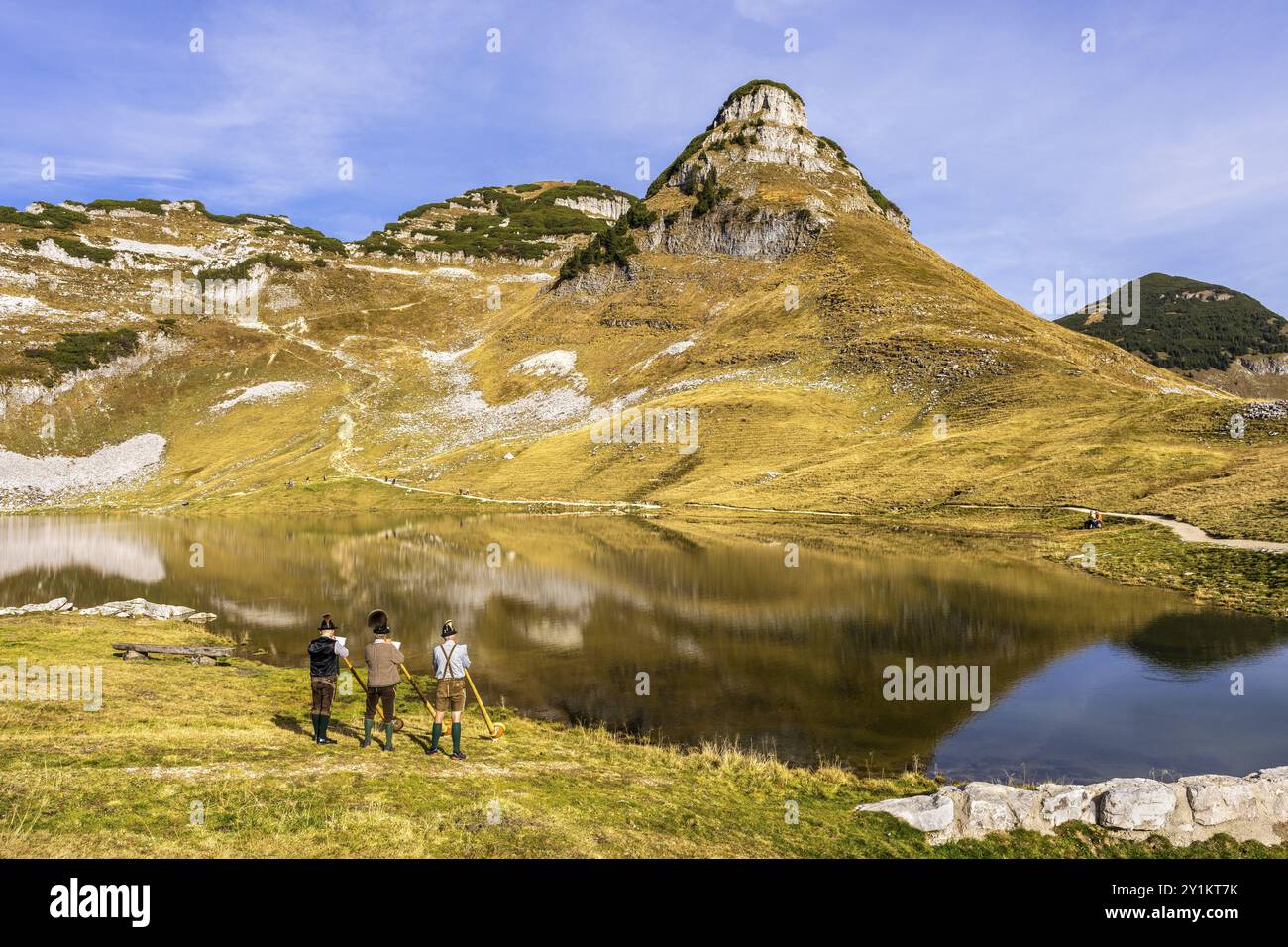 Drei Männer spielen das Alphorn am Augstsee am Mount Loser. Das österreichische Alphorntrio Klangholz. Der Atterkogel im Hintergrund. Herbst, gutes Wetter Stockfoto