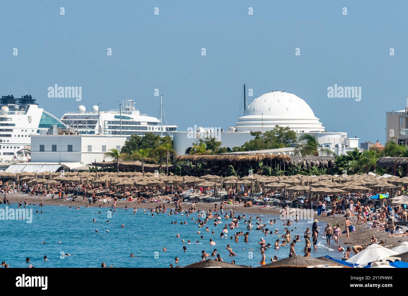 Rhodos-Stadt, Griechenland – 18. Juli 2024. Elli Beach in Rhodos-Stadt, Griechenland. Blick mit Menschen, Kreuzfahrtschiffen und Ronda Beach Restaurant und Disco Gebäude i Stockfoto
