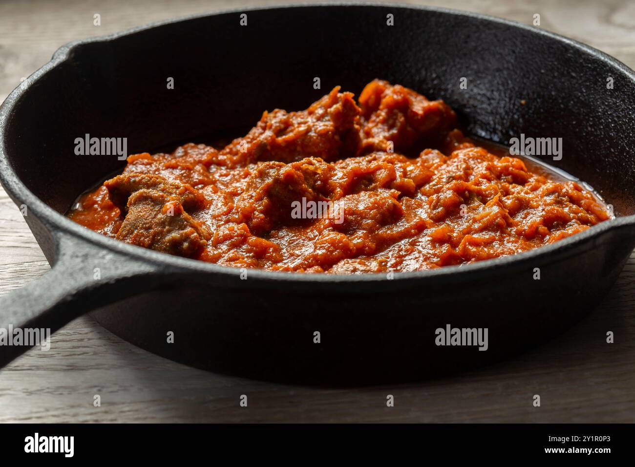 Rogan josh Lammcurry in einer gusseisernen Pfanne gekocht. Auf hölzernem Hintergrund Stockfoto