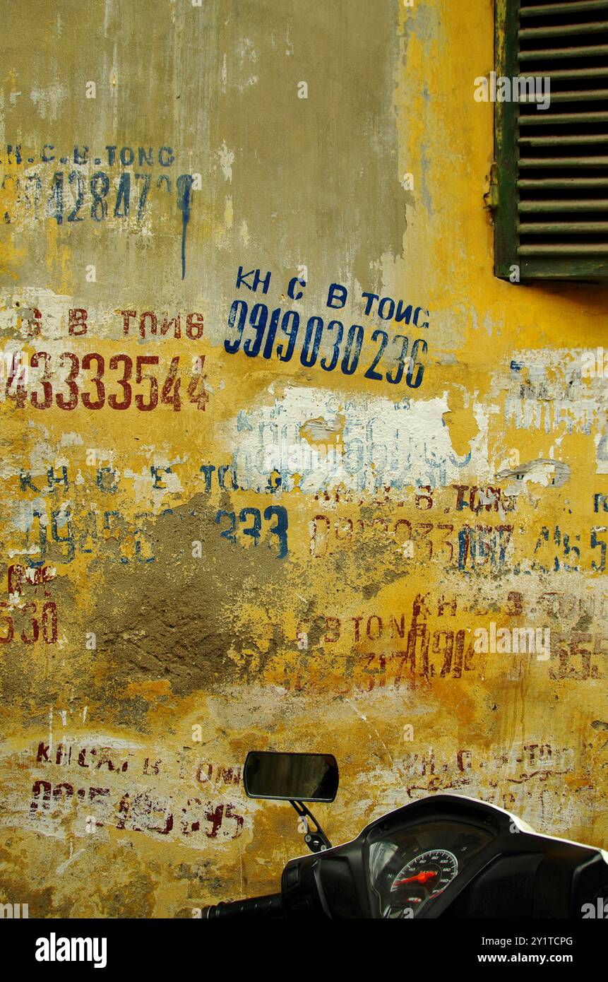 Alte gelbe Mauer in der Hanoi Tiny Street mit Telefonnummernmalerei. Stockfoto