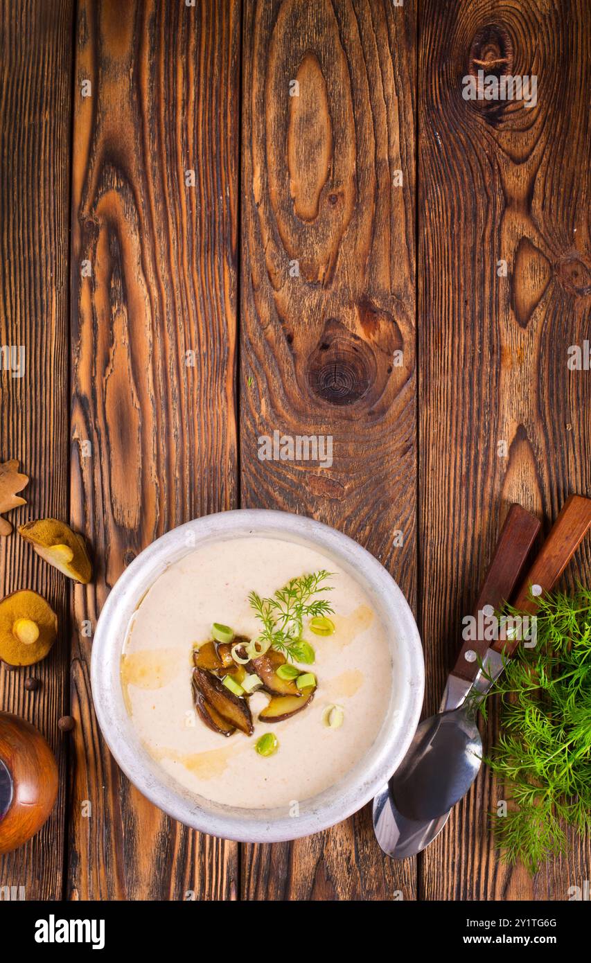 Auf dem Holztisch gibt es eine Cremesuppe mit frischen Pilzen als Basis, umgeben von frischem Gemüse. Stockfoto
