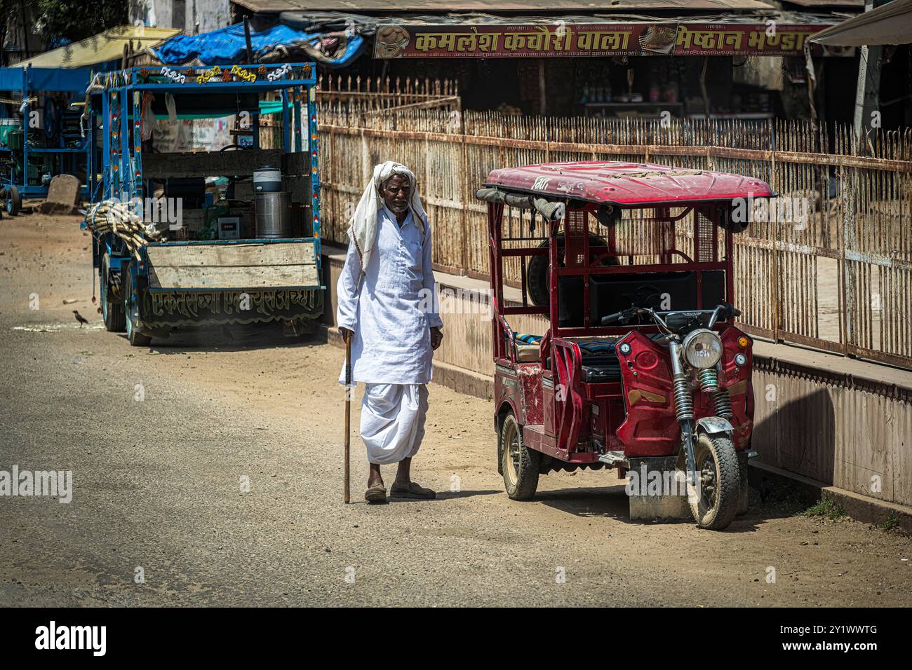Abhaneri Village, Indien – 13. April 2023. Ein älterer Indianer läuft an Fahrzeugen entlang, die am Straßenrand im Dorf Abhaneri geparkt sind. Stockfoto