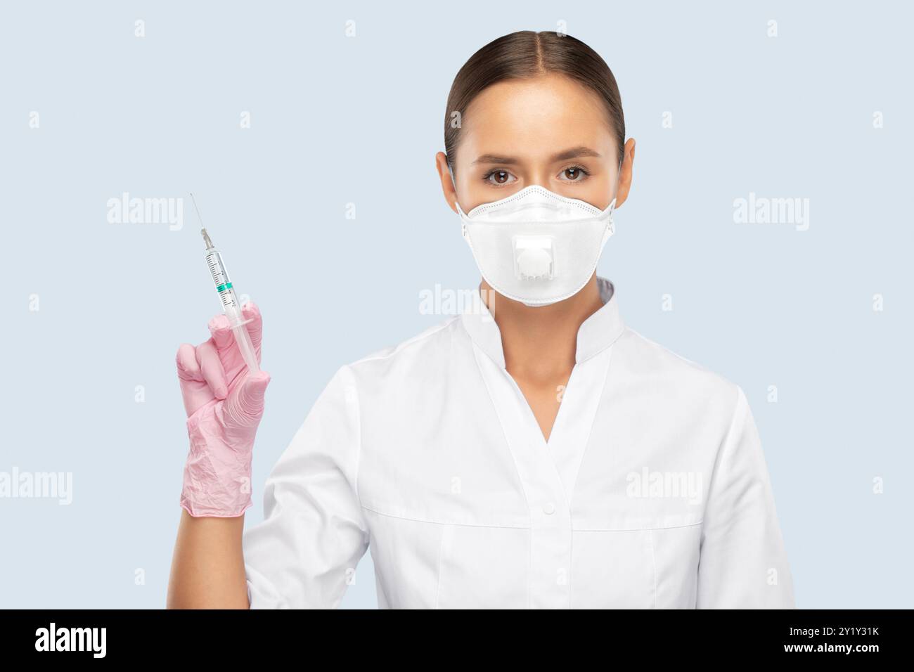 Ein Arzt in einem weißen Mantel, eine Gesichtsmaske, Gummihandschuhe hält eine Spritze mit einem Impfstoff in der Hand. Medizinisches Konzept, COVID-19. Stockfoto