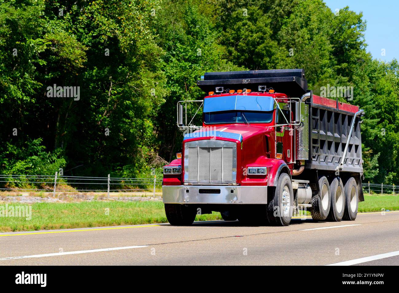 Horizontaler Schuss eines schweren roten Müllwagens, der die Autobahn hinunter fährt. Stockfoto