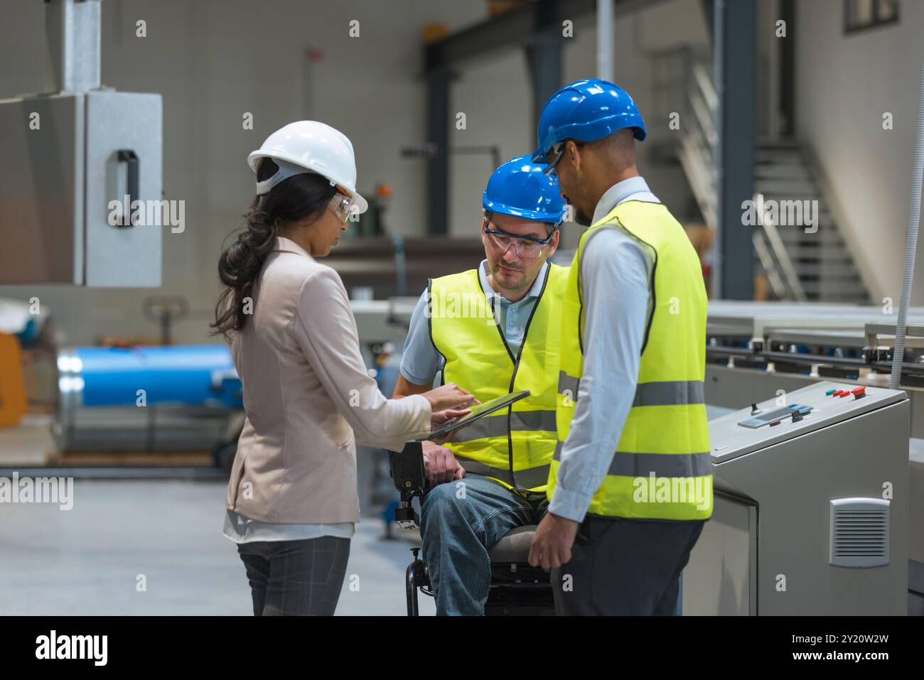 Weibliche Führungskraft spricht mit zwei Arbeitern an der Produktionslinie, darunter einer mit Behinderung, über den Produktionsprozess. Stockfoto
