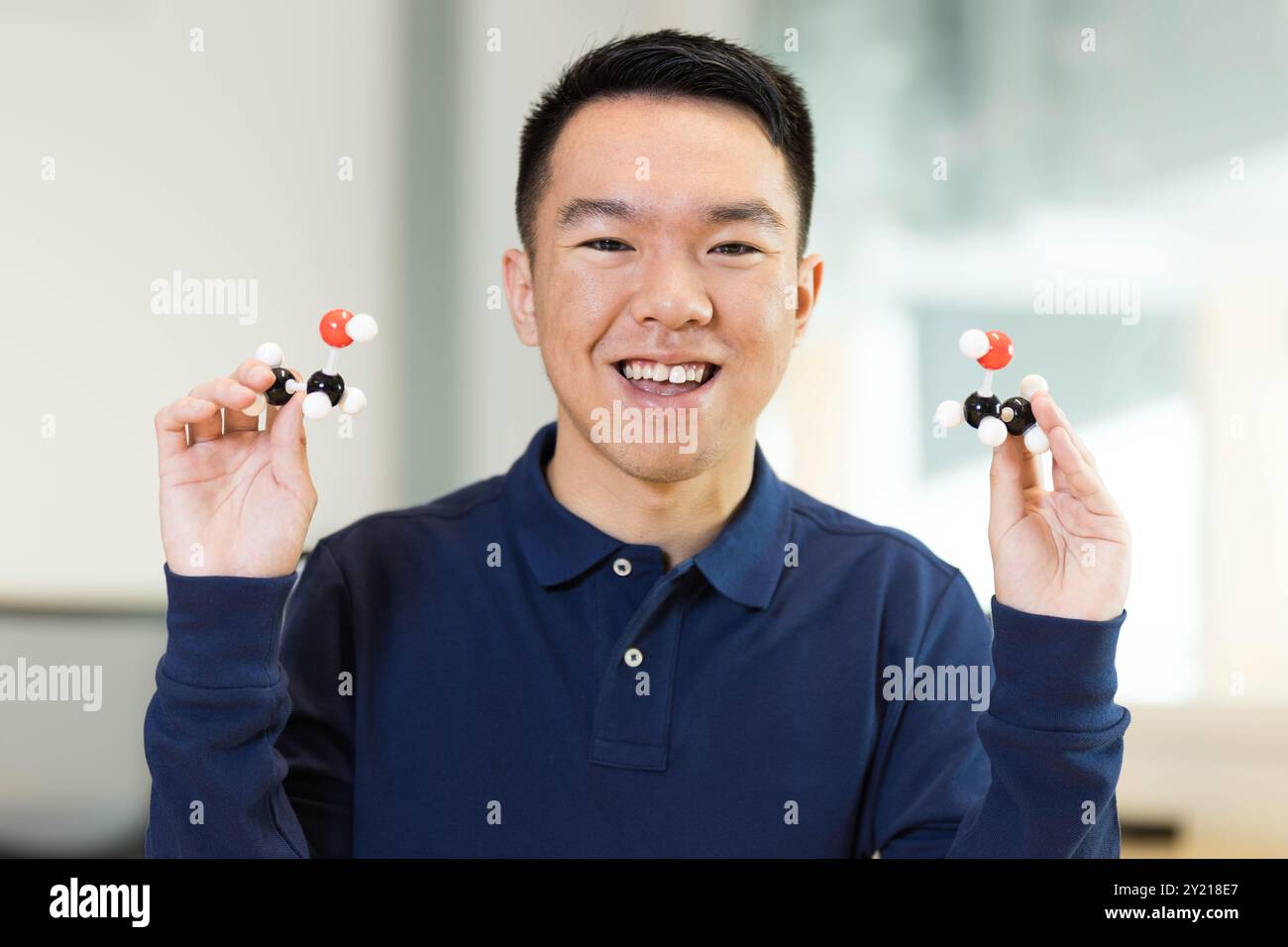 Ein junger Schüler hält ein Molekül-Modell hoch und lächelt in die Kamera im Klassenzimmer für den Chemiekurs. Stockfoto