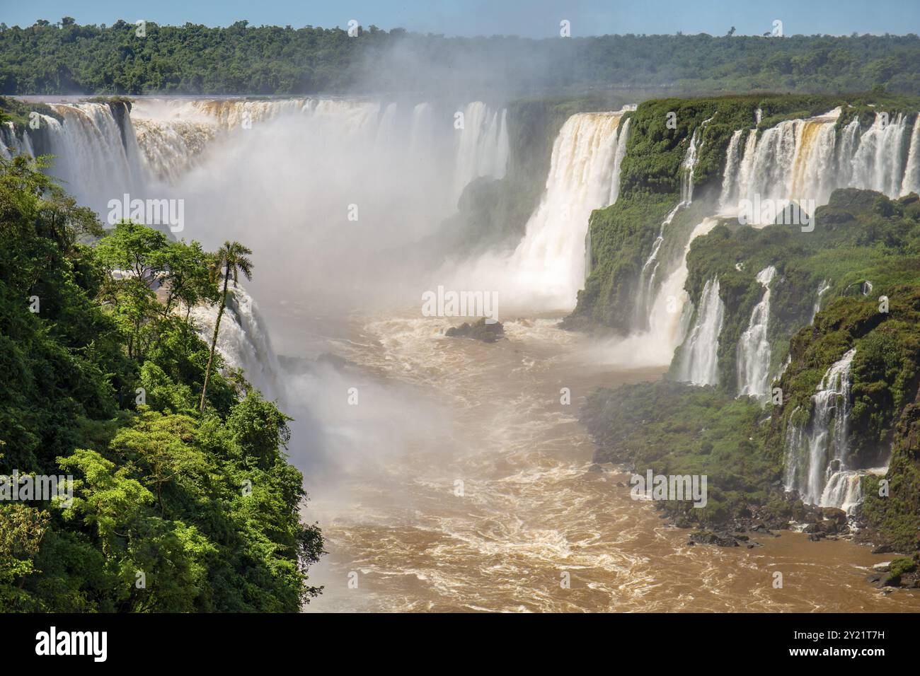 Blick auf Devil's Throat und die Schlucht der Iguazu Falls mit braunem Fluss, weißen Wasserfällen und üppigem grünen Regenwald bei Sonnenschein Stockfoto