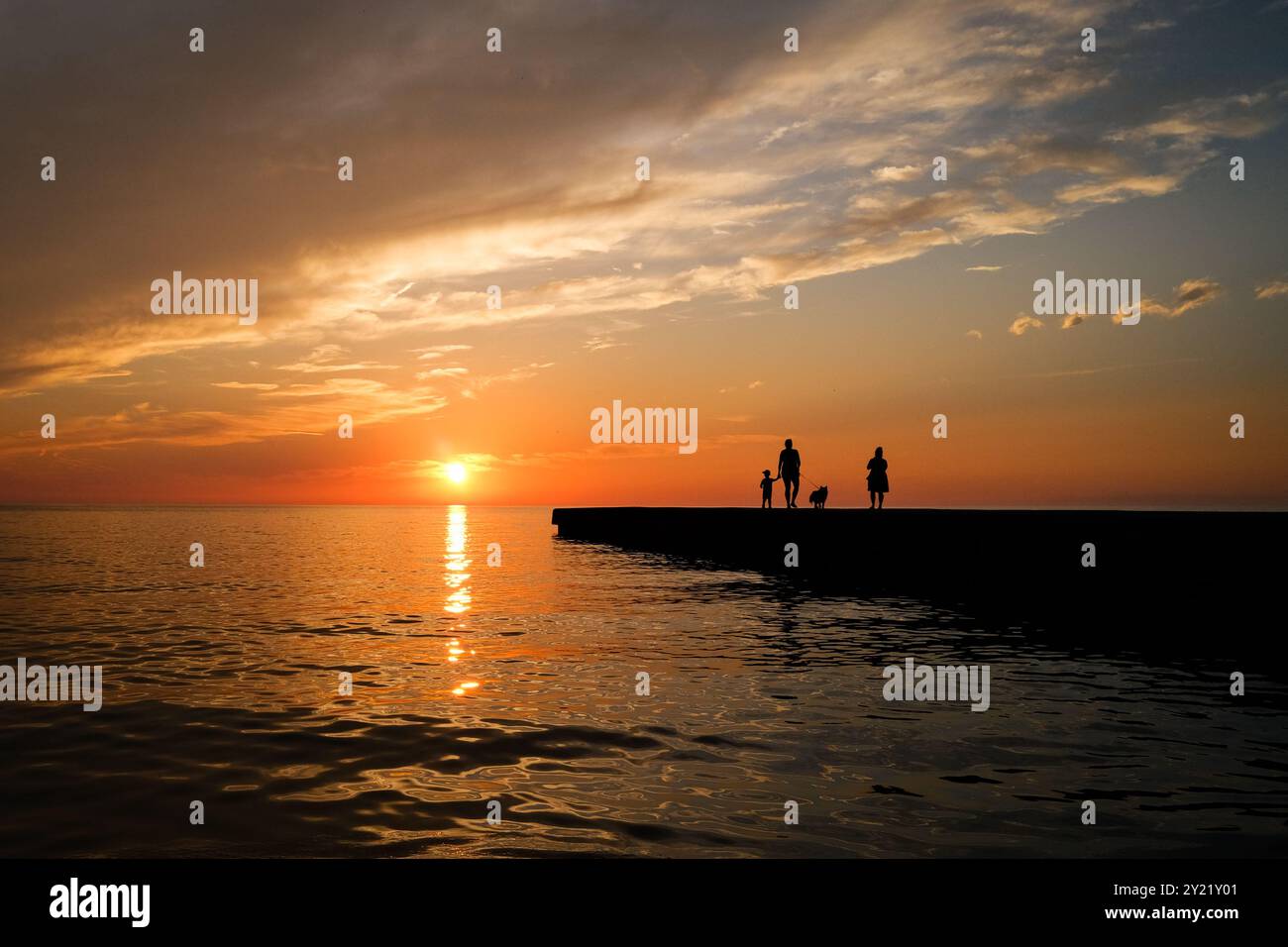 Sonnenuntergang vom Ufer des Ontario-Sees. Eine Familie, mit ihrem Hund, von der Sonne umrahmt, läuft am Pier entlang. Stockfoto