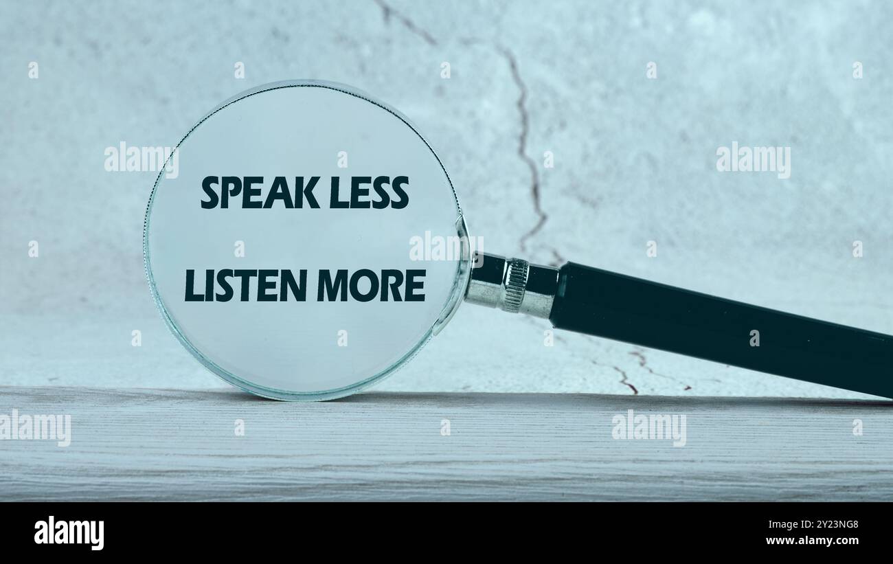 Sprechen Sie weniger, hören Sie mehr, Symbol. Konzeptwörter sprechen weniger Hören Sie mehr durch eine Lupe auf grauem Hintergrund Stockfoto