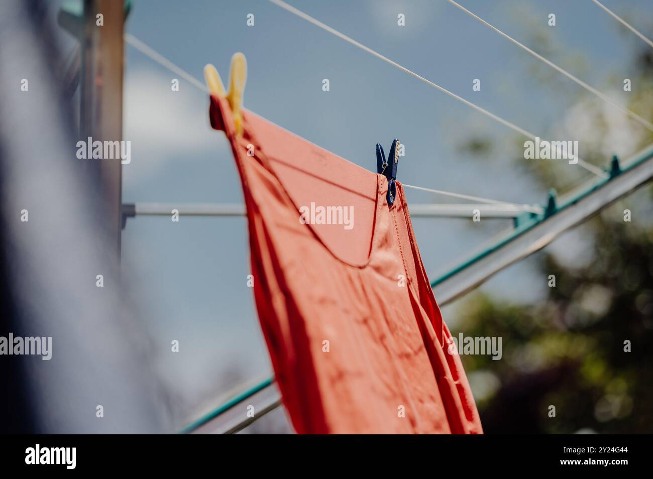 Rotes Kleidungsstück, das auf einer Wäscheleine trocknet, mit Kleiderschalen unter sonnigem Himmel Stockfoto