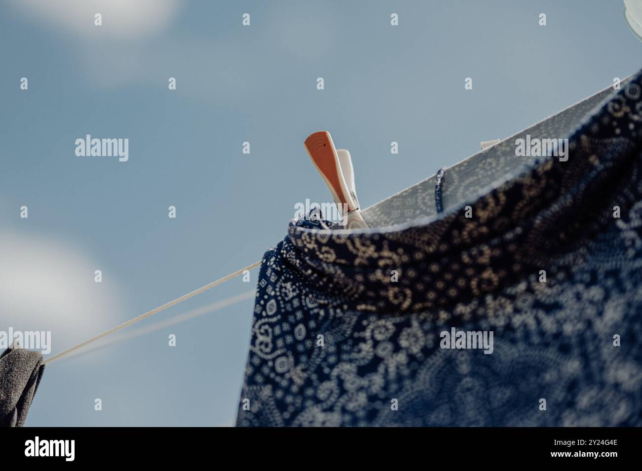 Blaues Kleidungsstück, das auf Wäscheleinen trocknet, mit Wäschespins unter sonnigem Himmel Stockfoto